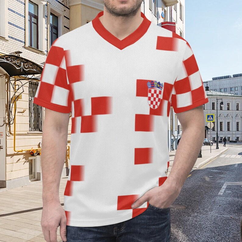 Op de afbeelding: Wit V-hals T-shirt met rood geblokt patroon en rode afwerking. Voorzien van een Kroatisch wapen op de borst. Het ontwerp van het shirt bevat de kleuren van de Kroatische vlag.