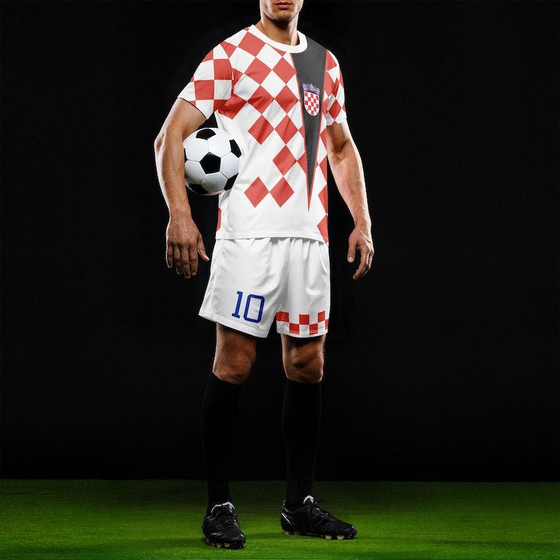 May include: A soccer uniform featuring a red and white checkered pattern on the jersey and shorts. The shorts have the number 10 in blue. The jersey has a black accent on the shoulder and a Croatian emblem. A soccer ball is held in the image.