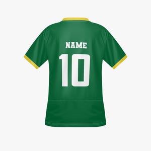 以下が含まれることがあります： 襟と袖に黄色のトリムが付いた緑色のスポーツジャージ。背中には、白いブロック体の数字10と、その上に「NAME」の文字が表示されています。ジャージは滑らかな、おそらく合成繊維で作られています。