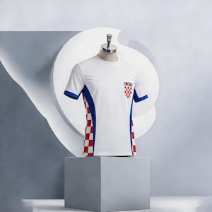 Peut inclure: T-shirt blanc avec des bordures bleues et l'embl&egrave;me des armoiries croates. Le t-shirt pr&eacute;sente un motif &agrave; carreaux rouges et blancs sur les c&ocirc;t&eacute;s. Les manches sont bord&eacute;es de bleu.