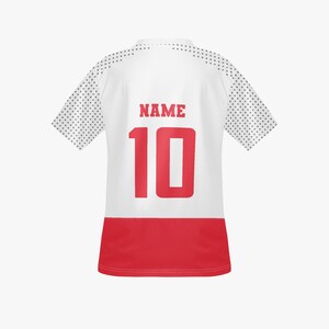 May include: White athletic jersey with red accents. The back features the word "NAME" above the number "10" in red. The sleeves have a dotted pattern. The bottom of the jersey is red.