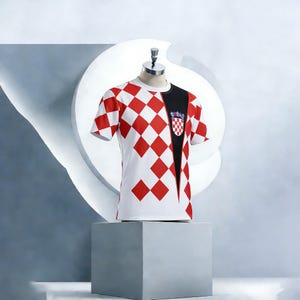 May include: A white t-shirt with a red and white checkerboard pattern on the front and sleeves. The shirt has a black panel on the right side with a crest. The shirt is displayed on a mannequin.