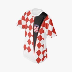 May include: A white t-shirt with a red and white checkered pattern on the sleeves and upper body. The shirt has a black vertical stripe down the front, with a Croatian coat of arms emblem.