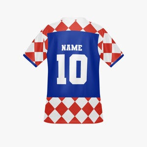 May include: A white and red checkered soccer jersey with a blue panel on the back. The jersey features the number 10 in white and the word "NAME" above it. The sleeves and lower portion of the jersey have a red and white diamond pattern.
