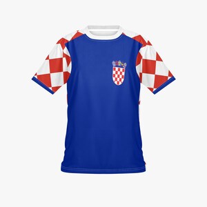 May include: A blue t-shirt with white sleeves featuring a red and white checkered pattern. The shirt has a white collar and a Croatian coat of arms emblem on the chest.