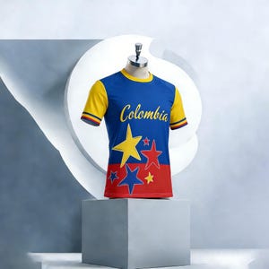 Op de afbeelding: Een blauw, geel en rood Colombia voetbalshirt met het woord "Colombia" in gouden letters. Het shirt heeft gele sterren en blauwe en rode accenten. Het shirt wordt op een mannequin gepresenteerd.