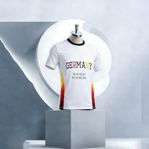 Op de afbeelding: Wit T-shirt met zwarte bies en het woord "GERMANY" in zwart, rood en geel. Het shirt heeft een ontwerp op de zijkanten met gele en rode verlopen. De tekst "You can add any text you want here" staat eronder.