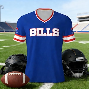 Könnte beinhalten: Ein blaues V-Ausschnitt-Trikot mit dem Wort "BILLS" in weißen Blockbuchstaben. Das Trikot hat rote und weiße Verzierungen an den Ärmeln und am Halsausschnitt. Ein Football und zwei schwarze Helme befinden sich im Vordergrund auf einem grünen Feld.