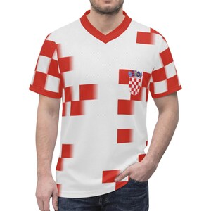 Op de afbeelding: Wit V-hals T-shirt met een rood-wit geblokt patroon. Het shirt heeft het Kroatische wapen op de borst. De mouwen en de halslijn zijn rood afgewerkt. Het ontwerp is gepixeld.
