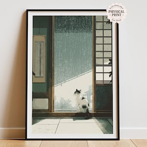 May include: Framed art print featuring a serene Japanese-style interior scene. A black and white cat sits by a large window, gazing out at a rainy day. The artwork includes traditional architectural elements and a hanging scroll. The print is in a black frame.