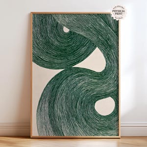 May include: A framed abstract art print with a swirling dark green design on a cream backdrop. The artwork has a minimalist style with flowing lines. The frame is made of light-coloured wood. Text on the upper right corner says "ALSO AVAILABLE PHYSICAL PRINT See Shop".
