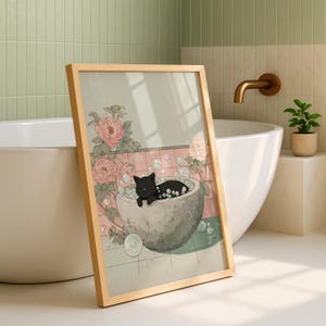 May include: A framed art print depicts a black cat relaxing in a stone tub filled with bubbles. The illustration features pink flowers and a light green and pink background. The frame is made of light-colored wood.