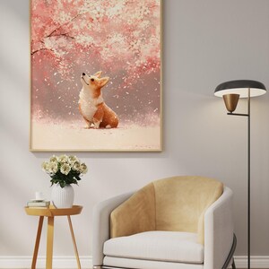 Puede incluir: Una impresi&oacute;n art&iacute;stica enmarcada con un perro corgi mirando hacia arriba a un cerezo en flor con flores rosas y blancas. La obra de arte se exhibe sobre un sill&oacute;n moderno y una mesa auxiliar con un jarr&oacute;n de rosas blancas.