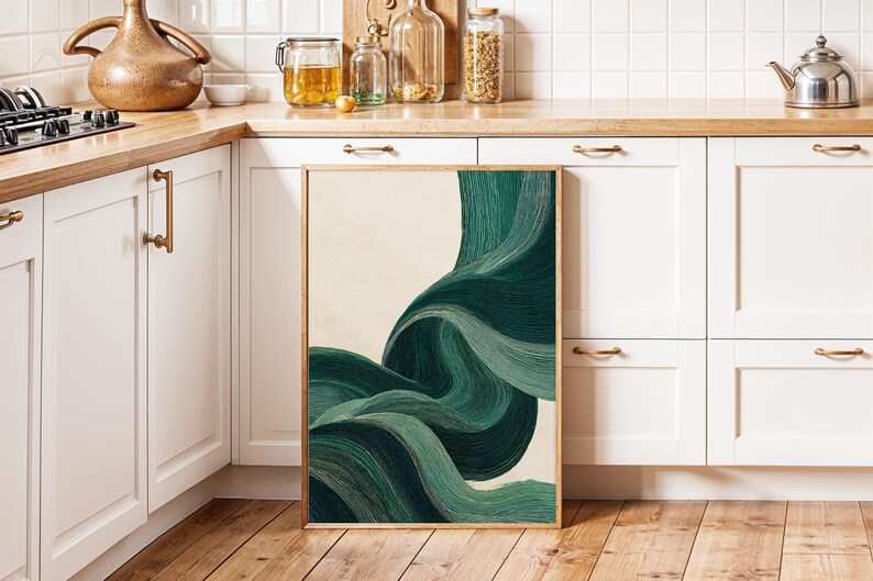 May include: A framed abstract art print featuring flowing, layered brushstrokes in shades of green and teal against a cream background. The artwork is displayed on a wooden floor, leaning against a white cabinet in a kitchen setting.