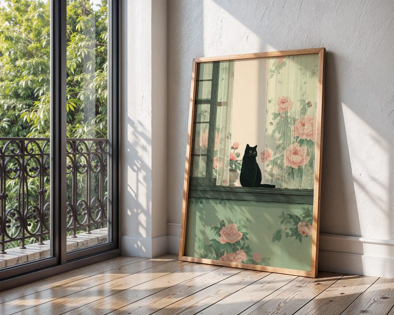 May include: A framed art print featuring a black cat perched on a windowsill. The artwork depicts a window with floral curtains and a pot of pink roses. The frame is made of light-colored wood, and the overall aesthetic is soft and inviting.