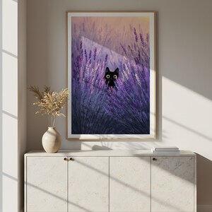 May include: A framed art print depicting a black cat amongst purple lavender. The cat has large, round eyes. The artwork is displayed above a white cabinet with a vase and dried flowers.