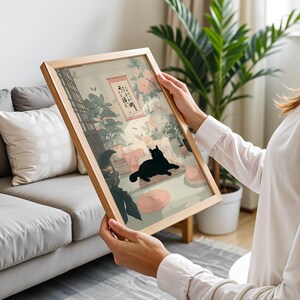 May include: A framed art print featuring a black cat lounging in a room with floral and plant decor. The artwork has a light wood frame and a soft color palette, with Japanese-inspired elements.