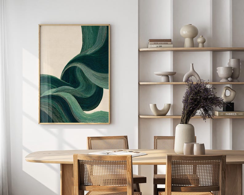 May include: A framed abstract art print featuring flowing, layered lines in shades of green and teal against a beige background. The artwork is displayed in a room with a wooden table and chairs, and a shelf with decorative items.