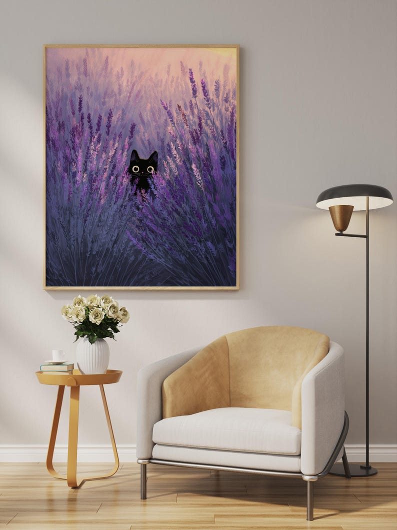 May include: A framed art print depicting a black cat amongst purple lavender. The artwork has a soft, painterly style with a warm, golden sky. The cat's eyes are wide and expressive. The print is displayed above a modern chair and side table.