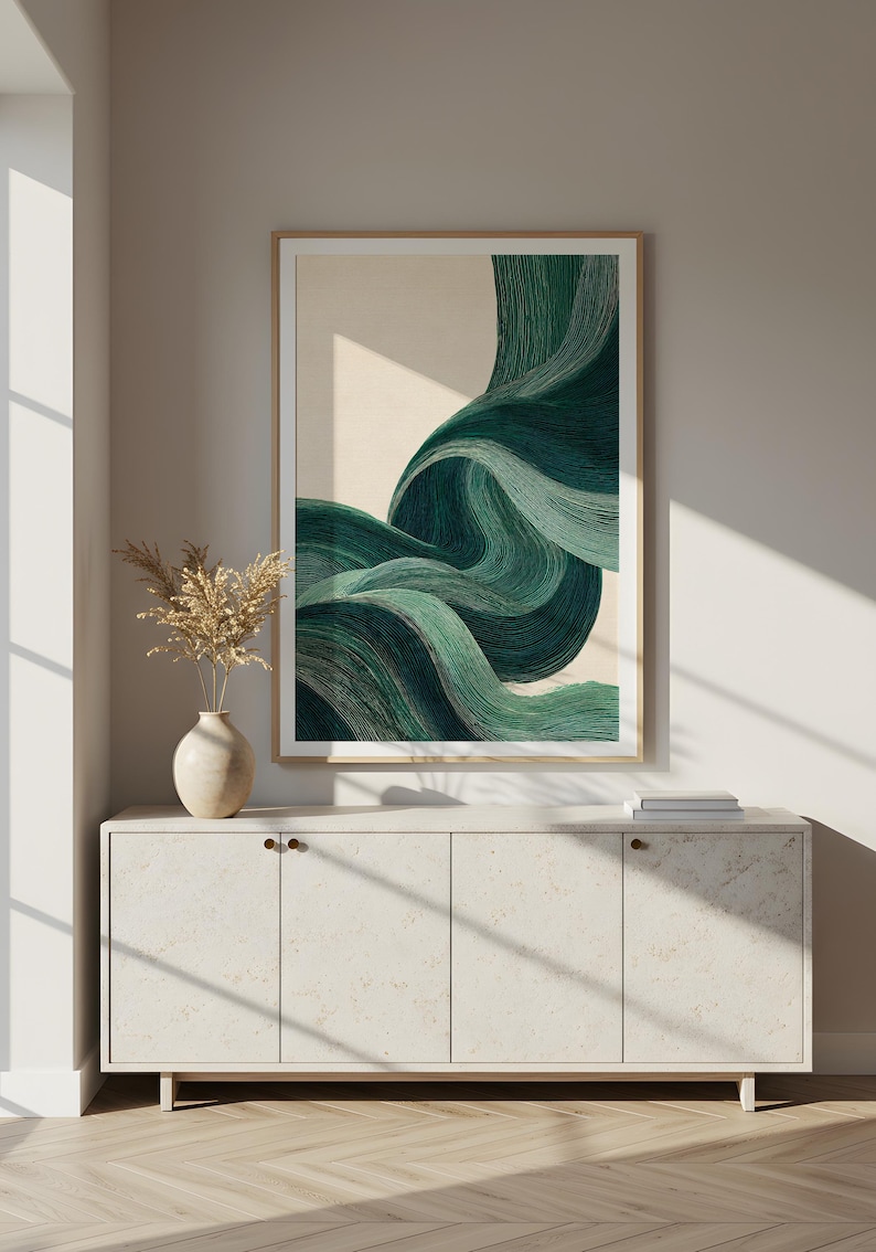 May include: Abstract art print featuring flowing, layered lines in shades of teal and green. The artwork is framed in a light wood frame and hangs above a white cabinet with a vase of dried flowers. The overall aesthetic is modern and minimalist.