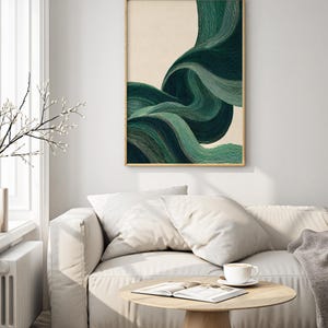 May include: Abstract art print featuring flowing, layered lines in shades of green against a cream background. The artwork is framed in a thin, gold-colored frame. The print hangs above a white sofa with pillows, a wooden coffee table, and a cup of coffee.
