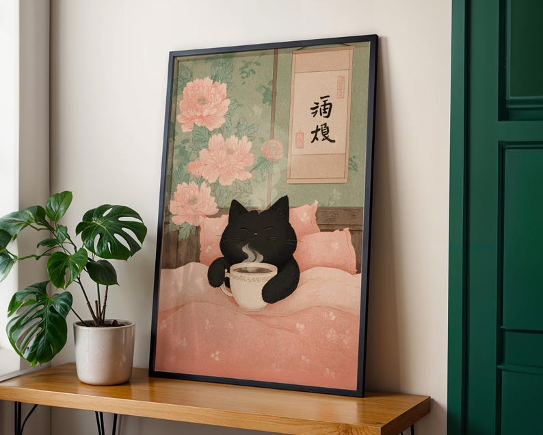May include: Framed art print featuring a black cat in bed, holding a steaming cup of coffee. The artwork has a Japanese aesthetic, with pink peonies and a scroll with Japanese characters. The cat is on a pink comforter.