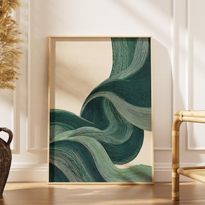 May include: Abstract art print featuring flowing, layered forms in shades of green and teal against a beige background. The artwork is framed in a gold-colored frame and leans against a white wall. A decorative vase with dried plants is on the left.