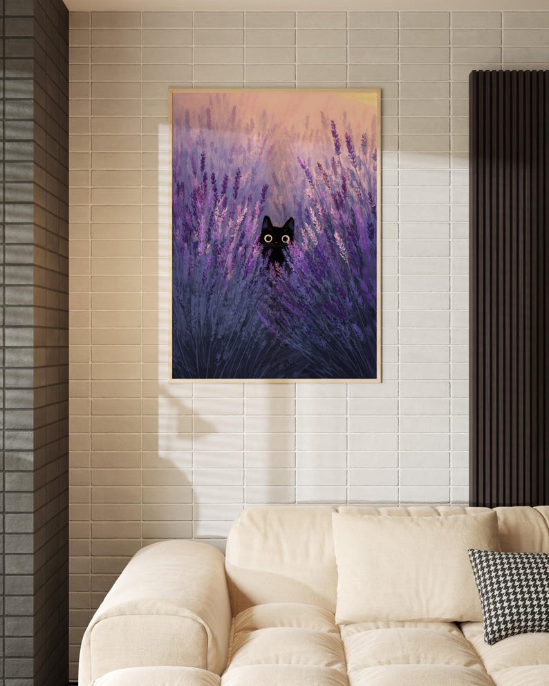 May include: A framed print depicting a black cat amongst purple lavender. The artwork has a soft, painterly style with a warm, sunset-coloured sky in the background. The frame is a light wood colour.