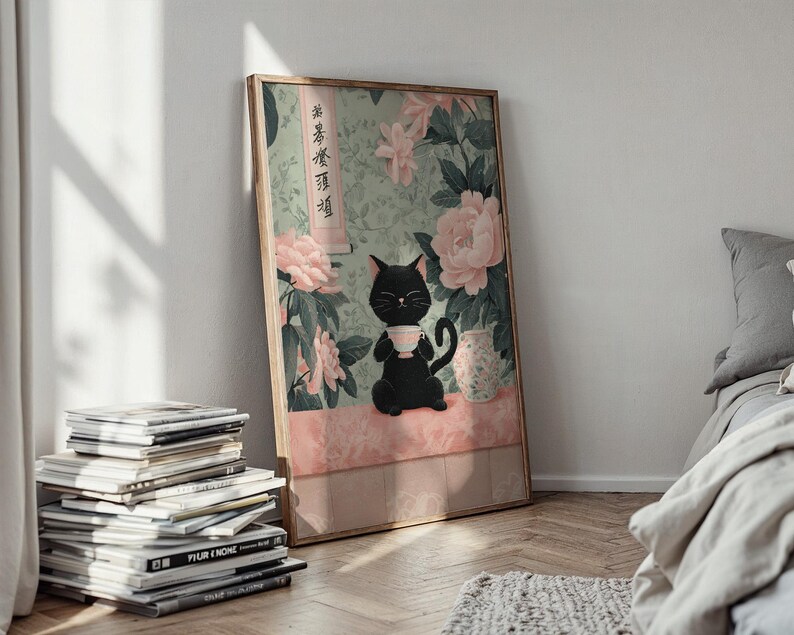 May include: A framed art print featuring a black cat holding a teacup, set against a backdrop of pink flowers and a light green background. The artwork has a vintage aesthetic, with Japanese text on the side. The print is leaning against a white wall.