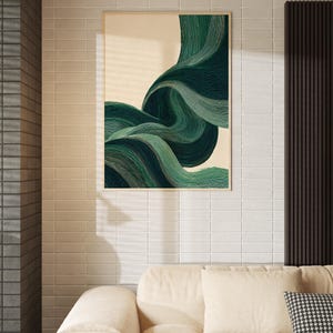 May include: A framed abstract art print featuring flowing, layered green and teal brushstrokes against a cream background. The artwork is displayed on a white tiled wall above a beige sofa with a patterned pillow.