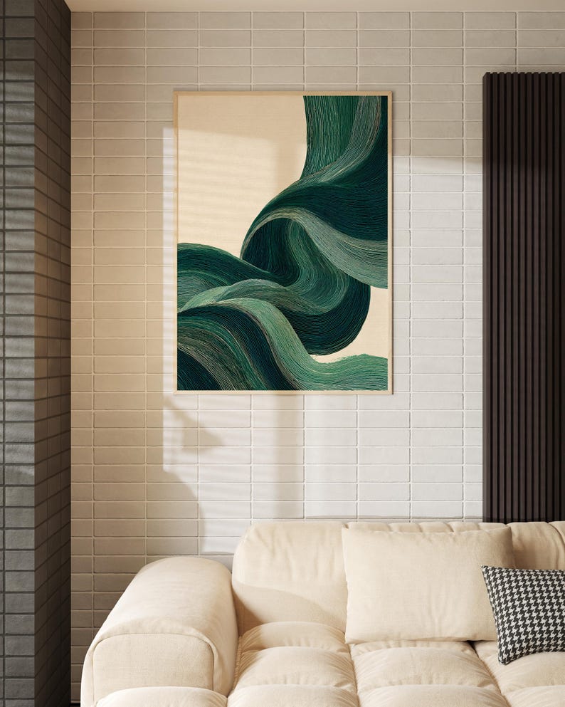May include: A framed abstract art print featuring flowing, layered green and teal brushstrokes against a cream background. The artwork is displayed on a white tiled wall above a beige sofa with a patterned pillow.
