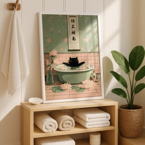May include: A framed art print depicts a black cat relaxing in a green bathtub filled with water and flowers. The artwork has a soft, pastel color palette with pink and green tones. A white towel hangs on a wooden hook, and a plant in a woven basket is on the right.