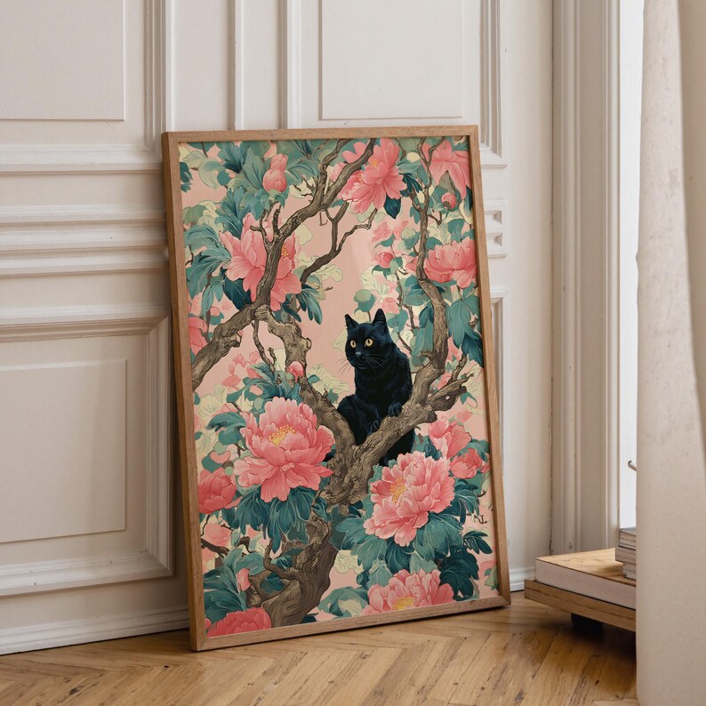May include: A framed art print featuring a black cat perched in a flowering tree. The artwork showcases a black cat with yellow eyes amidst pink peonies and green foliage against a soft pink background. The frame is a light brown color.