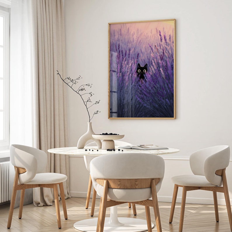 May include: A framed art print depicting a black cat in a lavender field. The artwork is in a wooden frame and hangs above a white table and chairs. The room has a neutral colour scheme with a white curtain.
