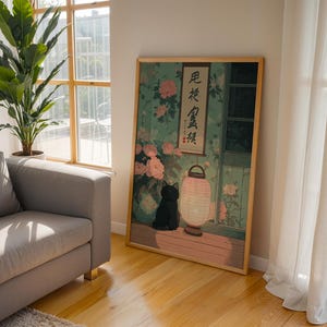 May include: A framed art print featuring a black cat, a paper lantern, and floral elements. The artwork is set against a backdrop of a window and a wall with floral patterns. The print has a wooden frame and is displayed on a wooden floor.