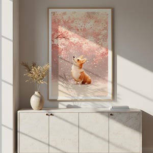 Puede incluir: Una impresi&oacute;n art&iacute;stica enmarcada con un perro corgi mirando hacia arriba, sobre un fondo de flores de cerezo rosas. La obra de arte se exhibe sobre un mueble blanco con un jarr&oacute;n de flores secas.