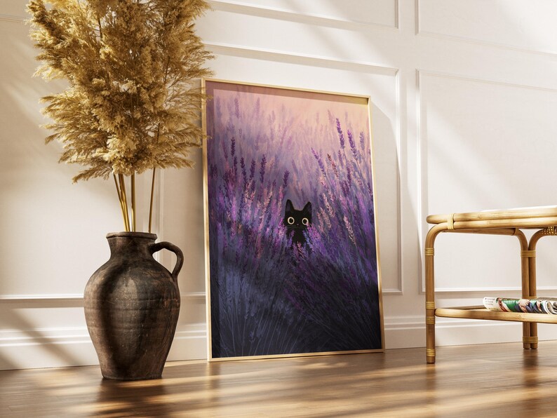 May include: A framed art print depicting a black cat in a lavender field. The artwork is in a gold frame, set on a wooden floor. A decorative vase with dried plants is to the left. The print is approximately 60 cm high.