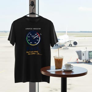 May include: A black short-sleeve t-shirt featuring a graphic of an airspeed indicator gauge with the text AIRSPEED INDICATOR, the word Fast, and the phrase Don't ask about the coffee with a small line drawing of a coffee mug next to the text.