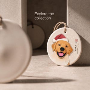 Editorial display of a personalized golden Labrador Christmas ornament in a minimal neutral setting, with the message “Explore the collection.”
