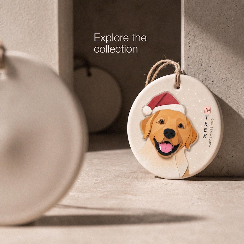 Editorial display of a personalized golden Labrador Christmas ornament in a minimal neutral setting, with the message “Explore the collection.”