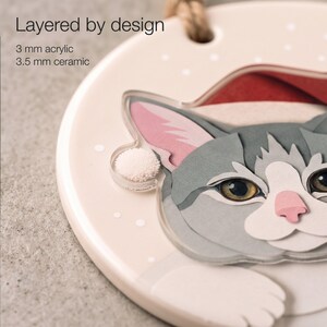 Close-up of a custom cat ornament showing the printed paper-cut shading, 3.5 mm ceramic base and separate 3 mm clear acrylic portrait layer.