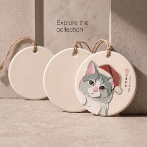 Editorial display of a personalized cat Christmas ornament in a minimal neutral setting, inviting shoppers to explore the pet portrait collection.