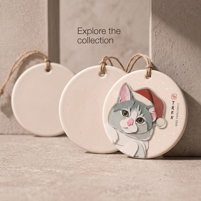 Editorial display of a personalized cat Christmas ornament in a minimal neutral setting, inviting shoppers to explore the pet portrait collection.