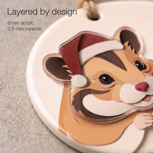 Close-up of a custom hamster ornament showing printed paper-cut shading, a 3.5 mm ceramic base and a separate 3 mm clear acrylic portrait layer.