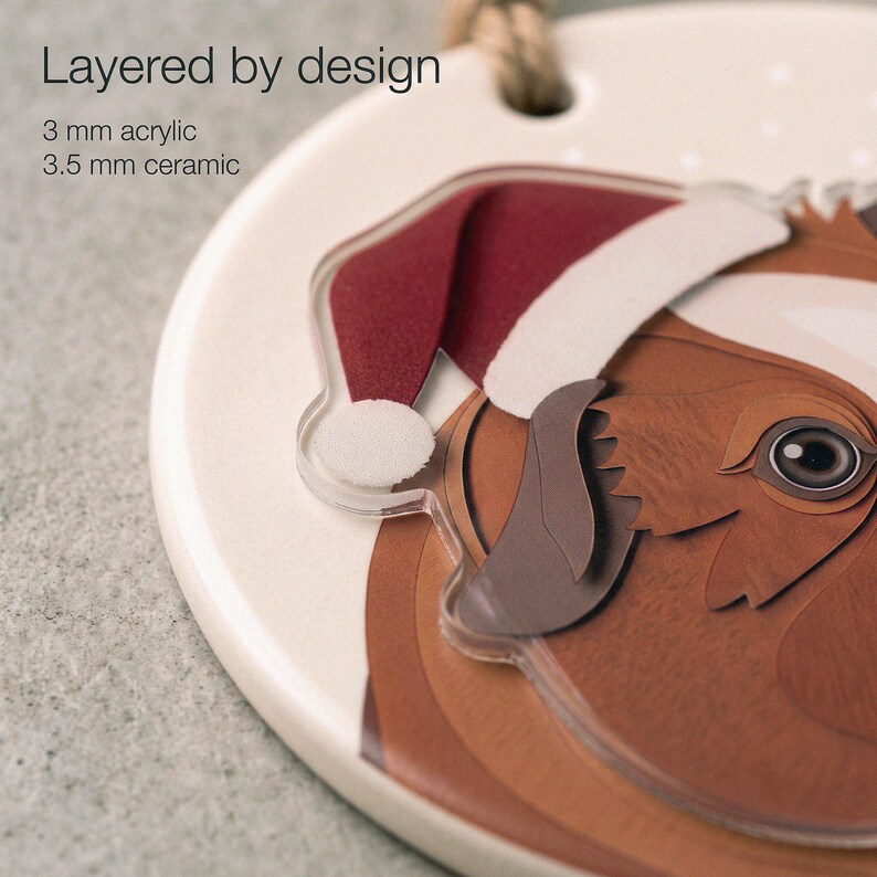 Close-up of a custom guinea pig ornament showing printed paper-cut shading, a 3.5 mm ceramic base and a separate 3 mm clear acrylic portrait layer.