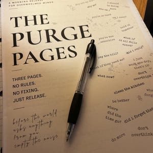 May include: A journal titled "The Purge Pages" with a black pen on top. The journal's cover features large, bold text and smaller text with phrases like "Three Pages. No Rules. Just Release." Scattered phrases like "clean the kitchen" and "don't overthink" are also visible.