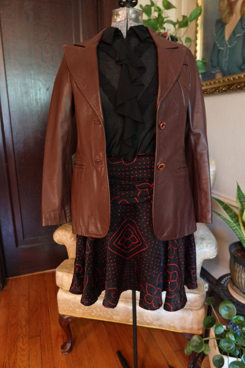 May include: A brown leather jacket with a black ruffled blouse and a black and red patterned skirt.