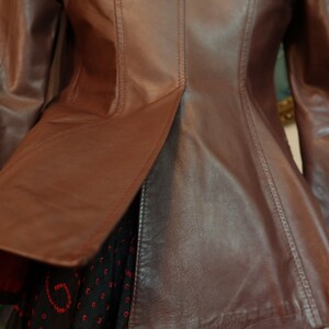 May include: A brown leather jacket with a fitted waist and a slightly flared hem. The jacket has a smooth, polished finish and features a seam down the back.