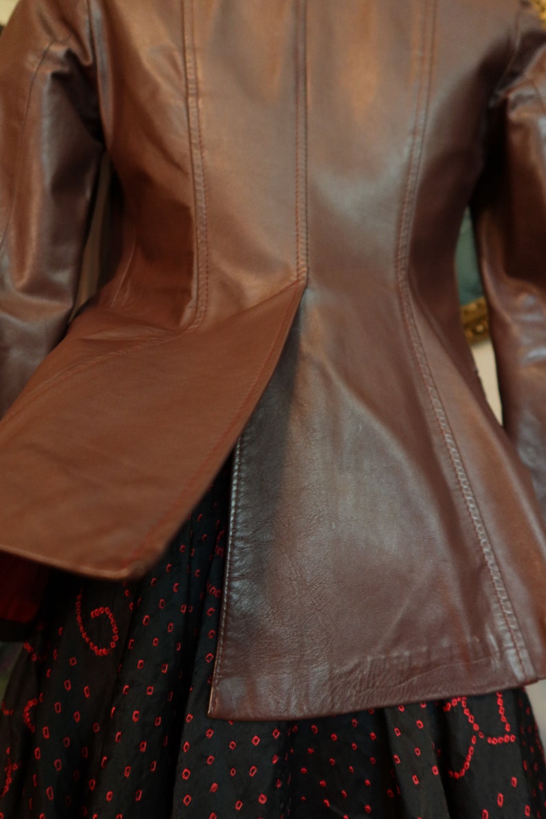 May include: A brown leather jacket with a fitted waist and a slightly flared hem. The jacket has a smooth, polished finish and features a seam down the back.