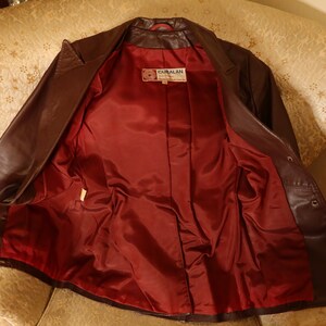 May include: A brown leather jacket with a red satin lining. The jacket has a button closure and a label that reads "GIBRALAN".